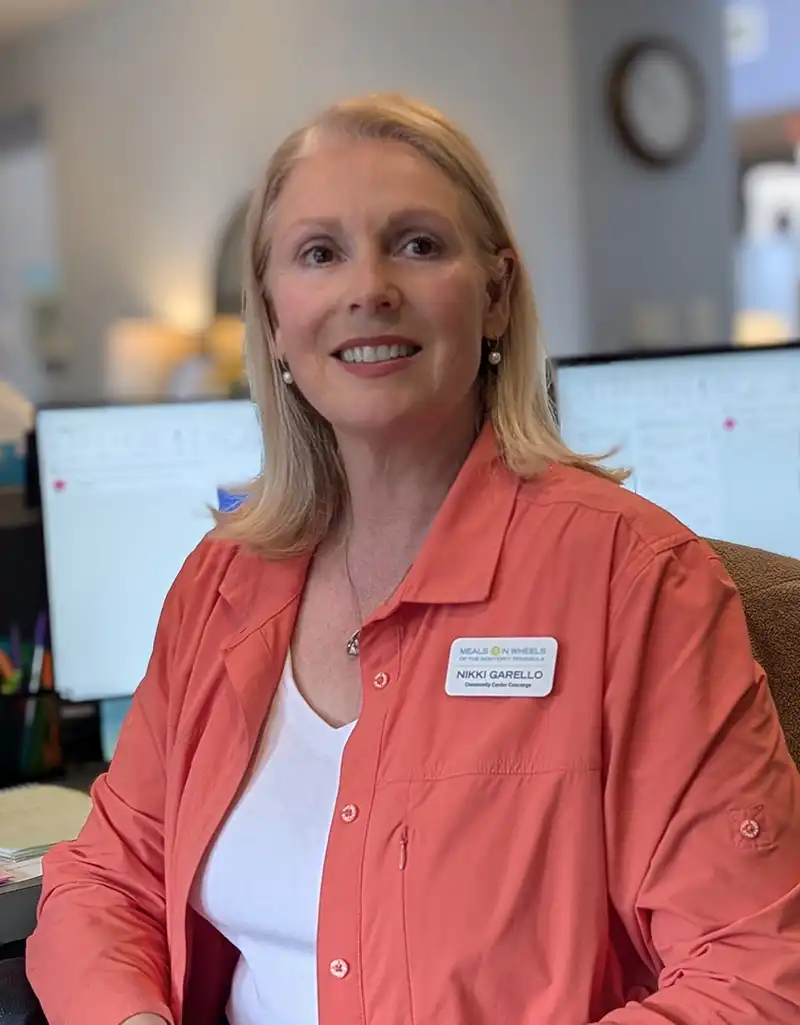 Community Center Concierge Nikki Garello smiling at her desk inside the Meals on Wheels Community Center office.