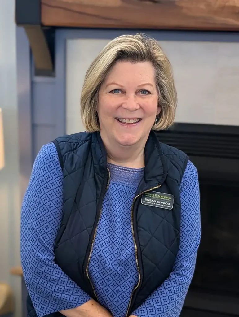 Recruitment and Outreach Manager Susan Elwood smiling in a Meals on Wheels of the Monterey Peninsula vest inside the Meals on Wheels Community Center.