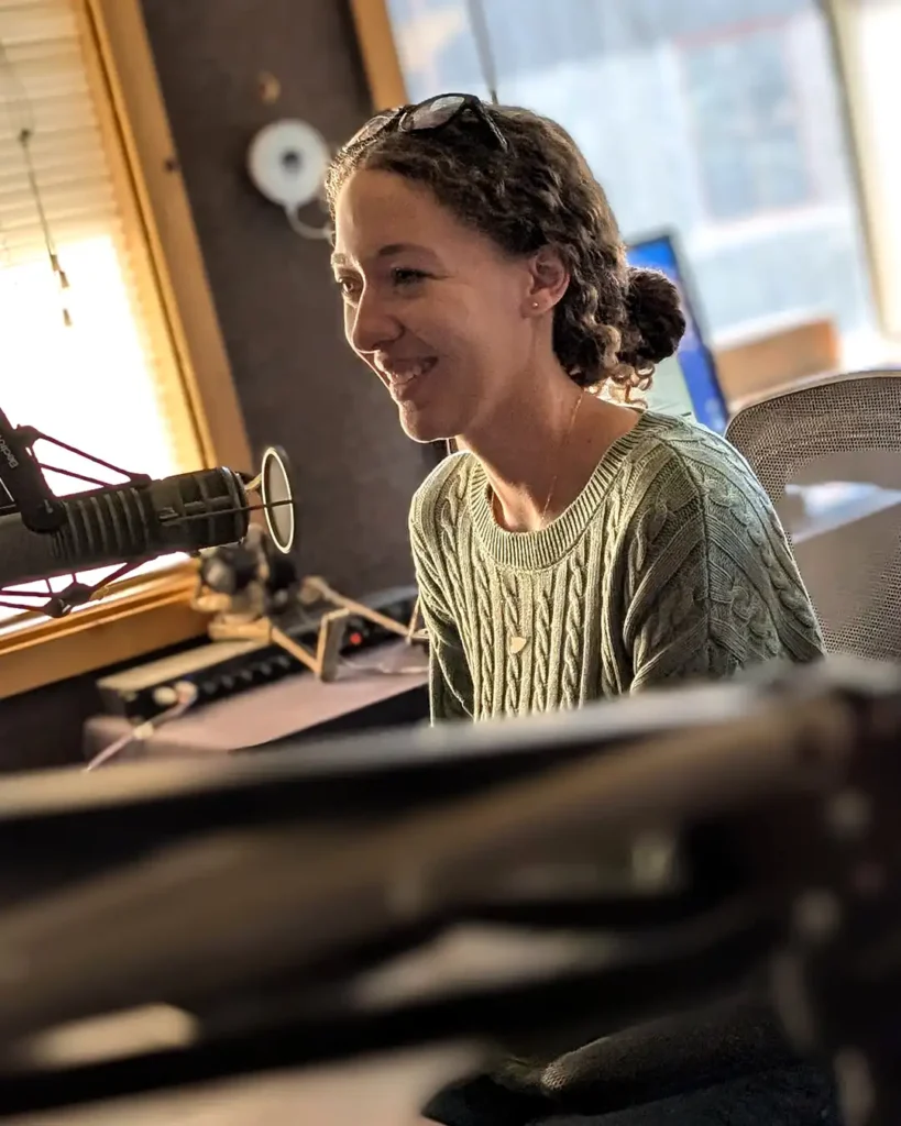 Home Delivered Meals Coordinator Carly Burgess speaking into a microphone while seated in a radio studio during a Meals & Feels recording.