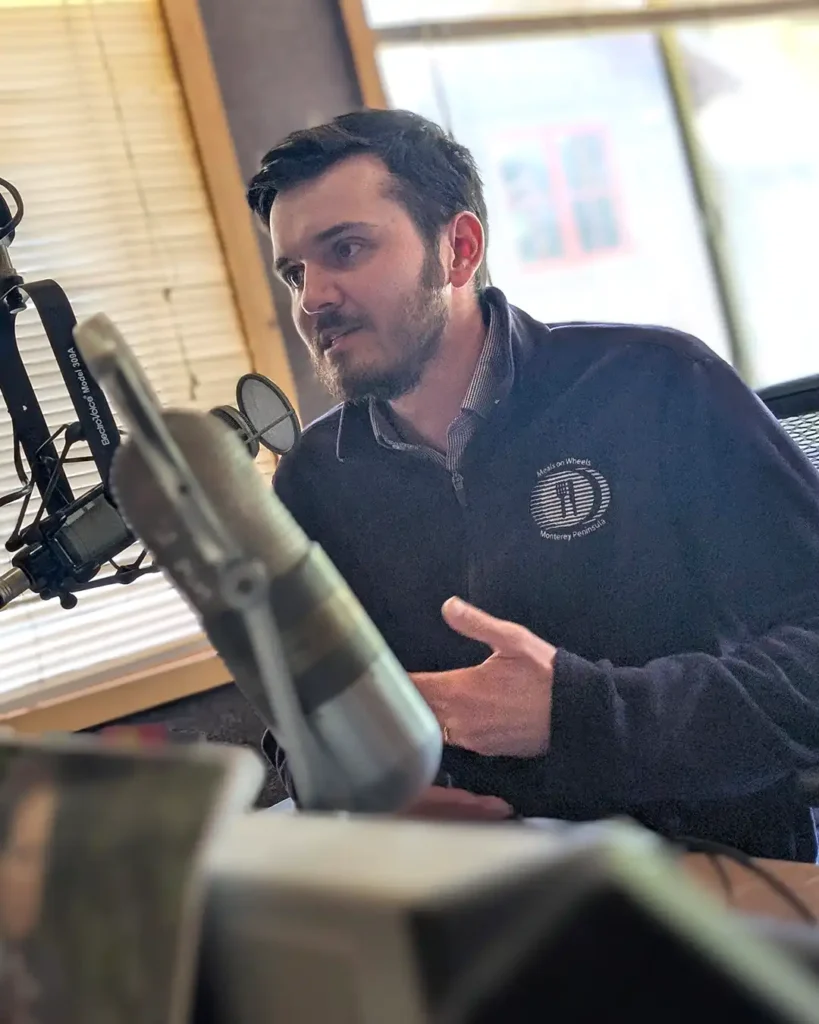 Home Delivered Meals Manager David Foster speaking into a microphone during a radio studio recording for the Meals & Feels weekly podcast.