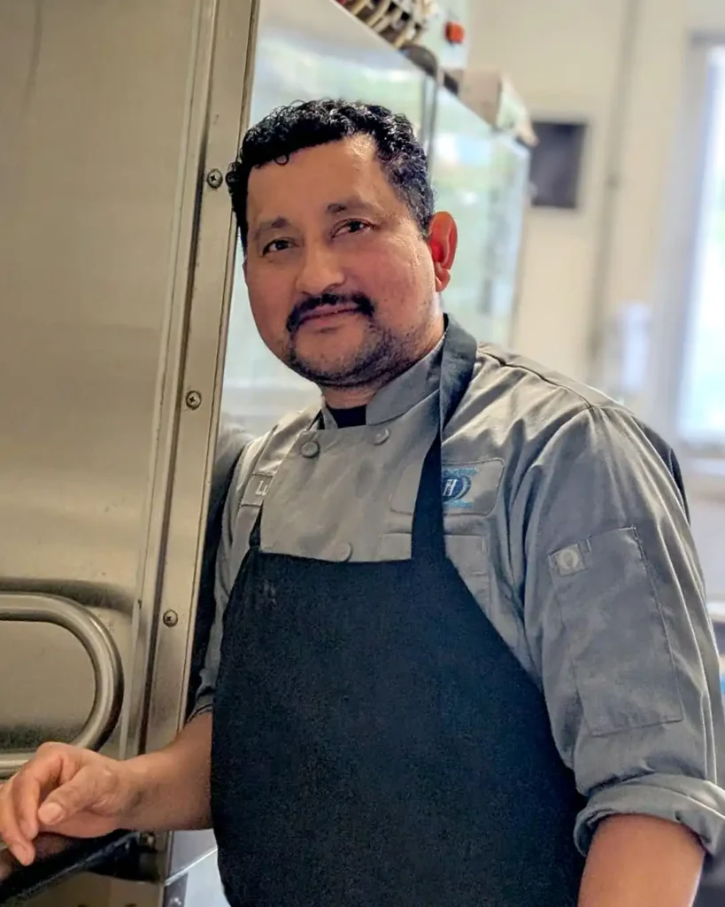 Portrait of Luis Garcia, cook at Meals on Wheels of the Monterey Peninsula, wearing a kitchen uniform and smiling.