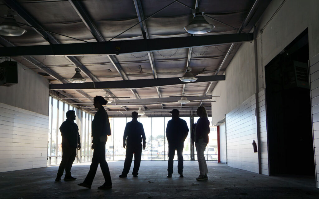 Meals on Wheels of the Monterey Peninsula team members standing inside the purchased building during a site visit, discussing use of an open interior space.