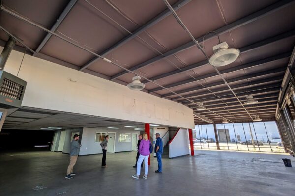 Meals on Wheels of the Monterey Peninsula team members standing inside the purchased building, reviewing an open main level space with concrete flooring and large windows.