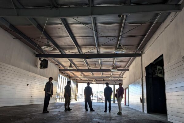 Meals on Wheels of the Monterey Peninsula team members standing inside the purchased building, reviewing an open main level space with concrete flooring and large windows.