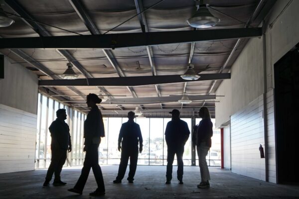 Meals on Wheels of the Monterey Peninsula team members standing inside the purchased building, reviewing an open main level space with concrete flooring and large windows.