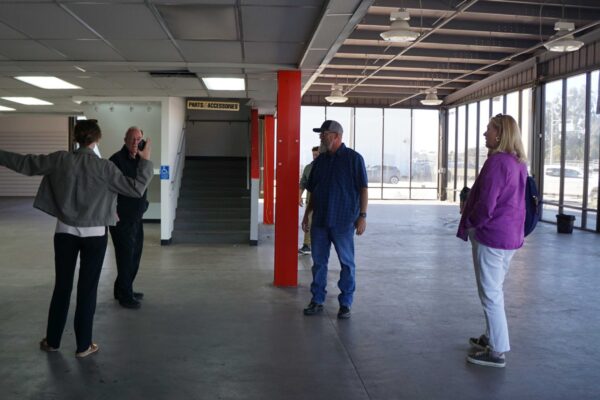 Meals on Wheels of the Monterey Peninsula team members standing inside the purchased building, reviewing an open main level space with concrete flooring and large windows.